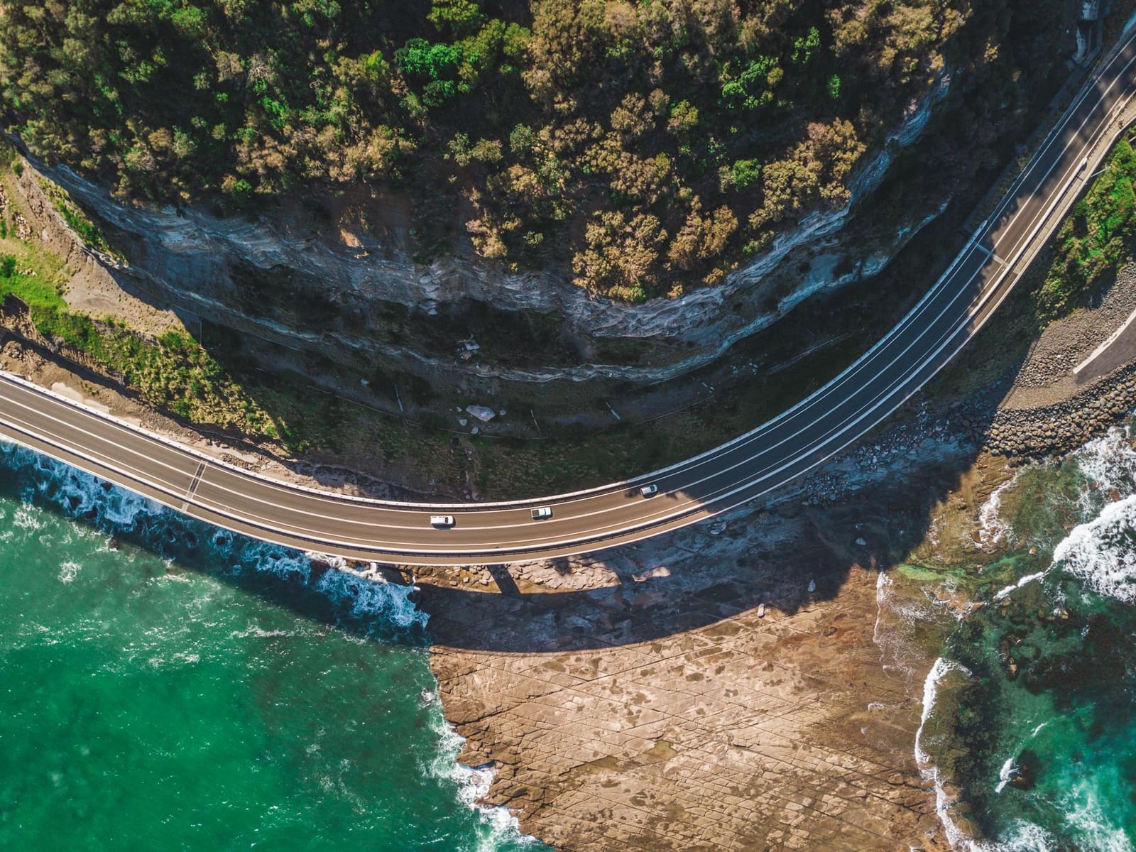 A coastal road winding along the shoreline between towns on the South Coast.