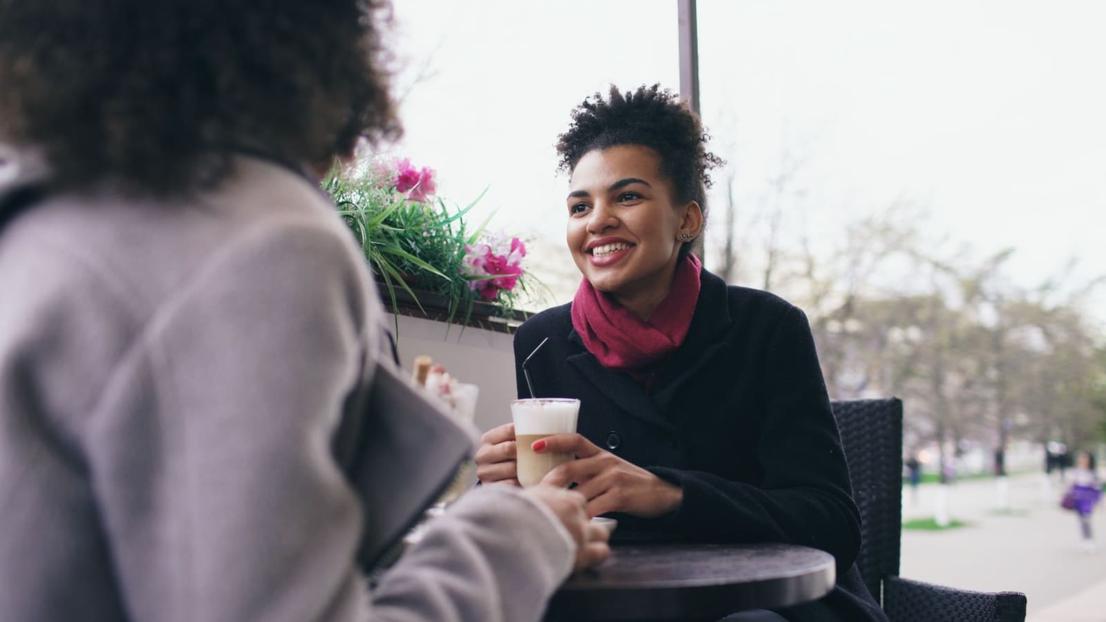 Two people talking and laughing over coffee at an outdoor cafe table.